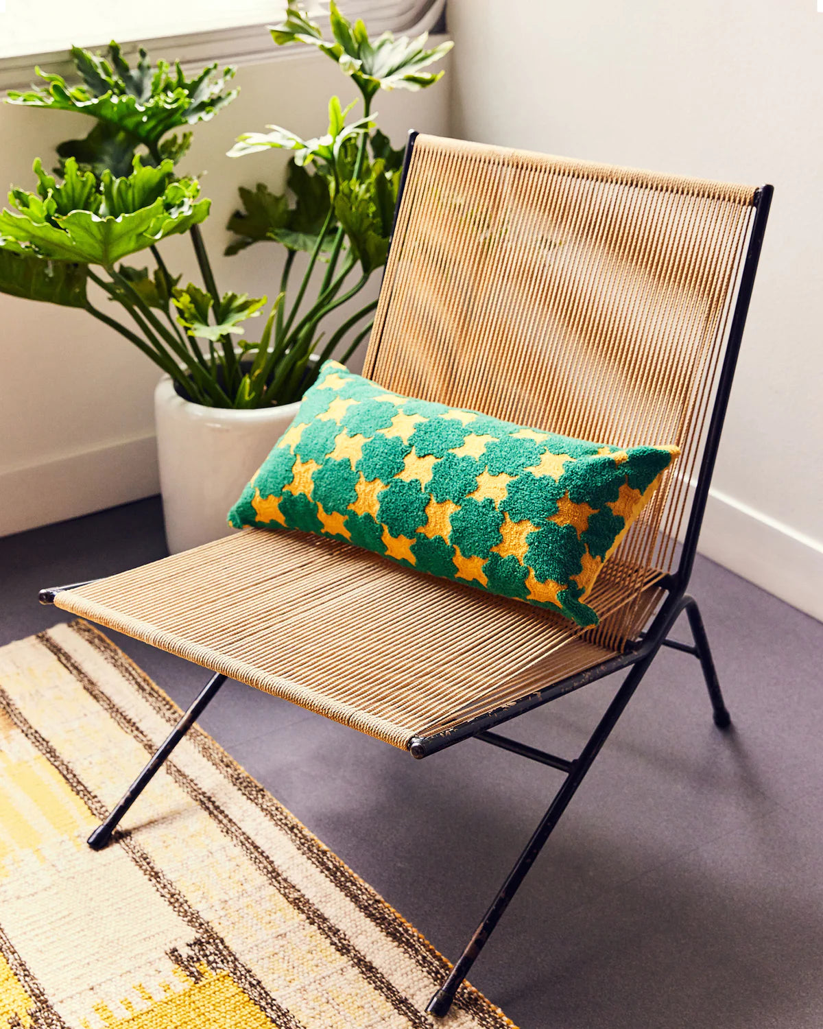 coussin graphique retangulaire dusen dusen bleu et jaune posé sur une chaise dans une pièce bohème avec des plantes