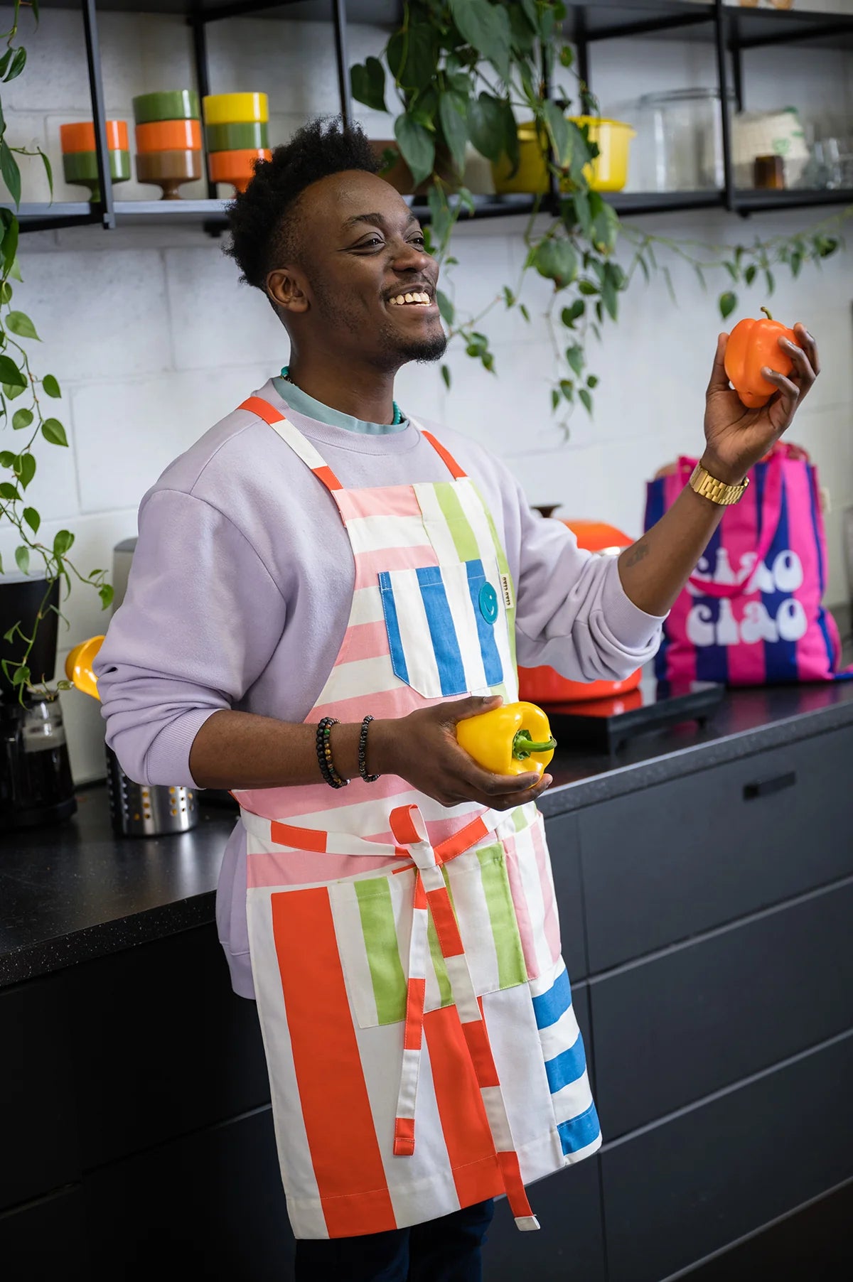 homme souriant en cuisine avec tablier Ciao Ciao et poivrons dans les mains