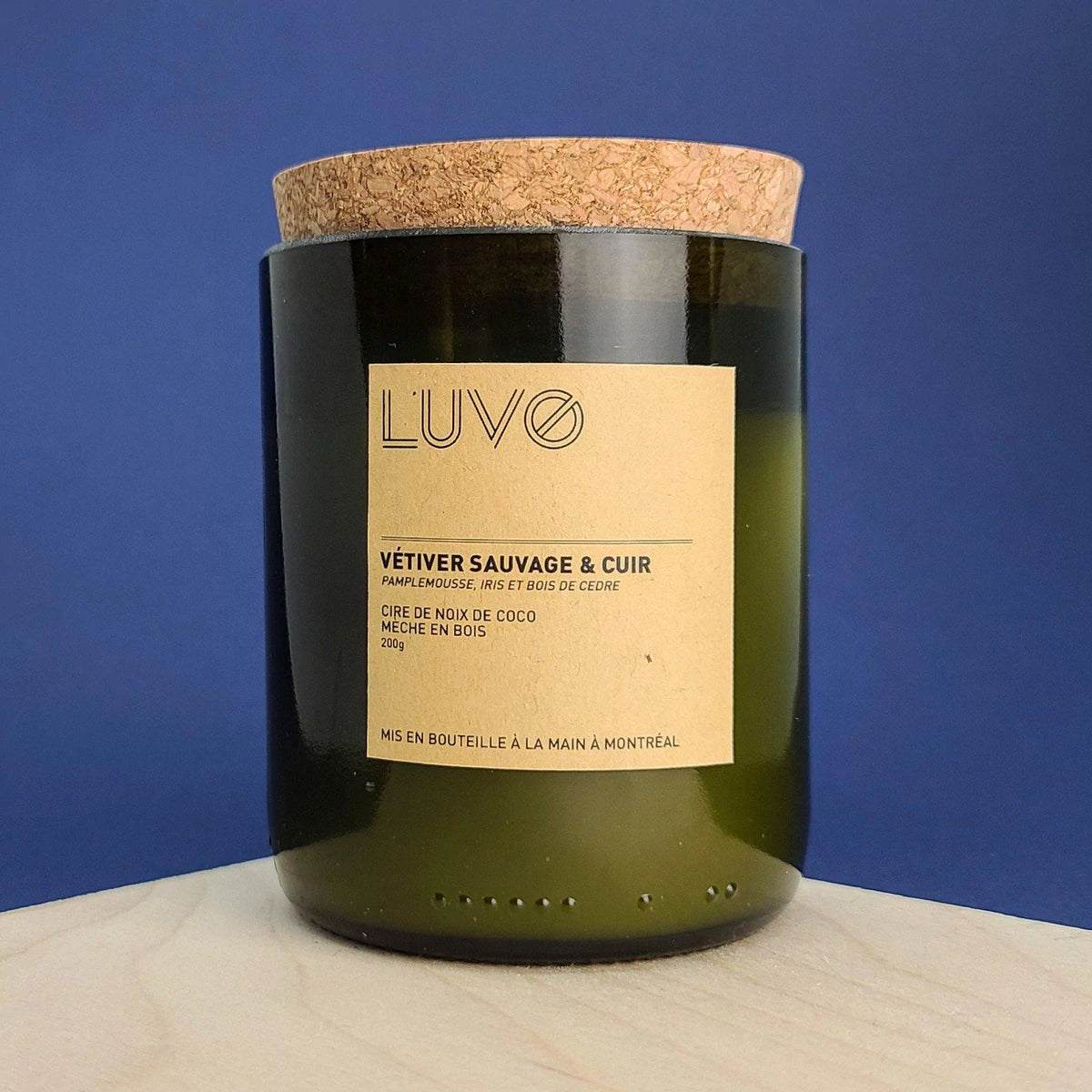 bougie Luvo parfumée vétiver sauvage et cuir. Bougie dans un bocal de bouteille de vin et bouchon en liège sur fond bleu foncé