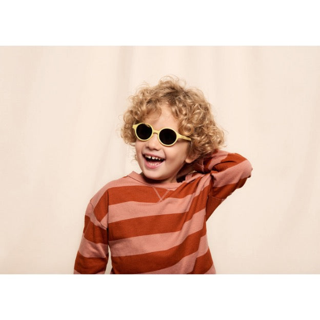 enfant souriant aux cheveux bouclées au pull rayé portant les lunettes jaune sun kids Izipizi